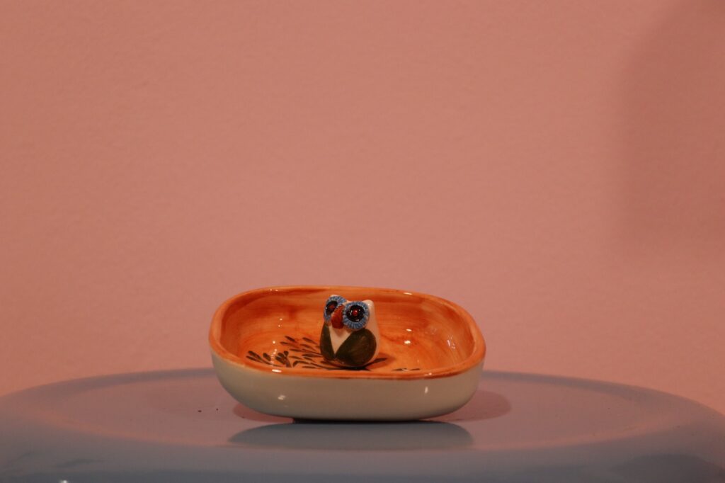 جا عودی سرامیکی دست‌ساز با طرح جغد کوچک داخل یک بشقابچه لعاب‌دار نارنجی و کرمی