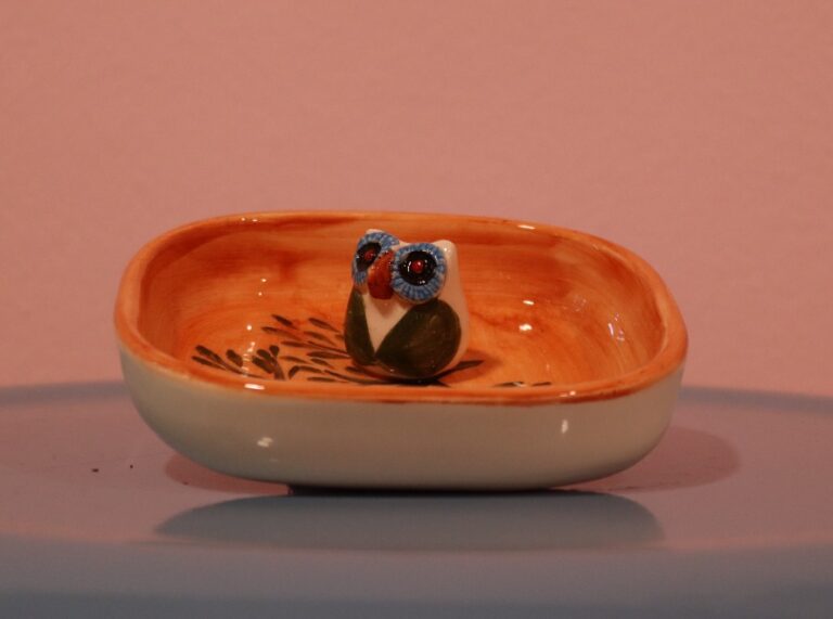 جا عودی سرامیکی دست‌ساز با طرح جغد کوچک داخل یک بشقابچه لعاب‌دار نارنجی و کرمی