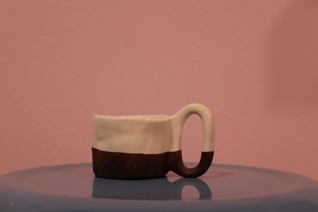 ماگ سرامیکی دست‌ساز دو رنگ با بدنه سفید و قهوه‌ای روی پس‌زمینه صورتی.