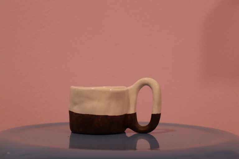 ماگ سرامیکی دست‌ساز دو رنگ با بدنه سفید و قهوه‌ای روی پس‌زمینه صورتی.